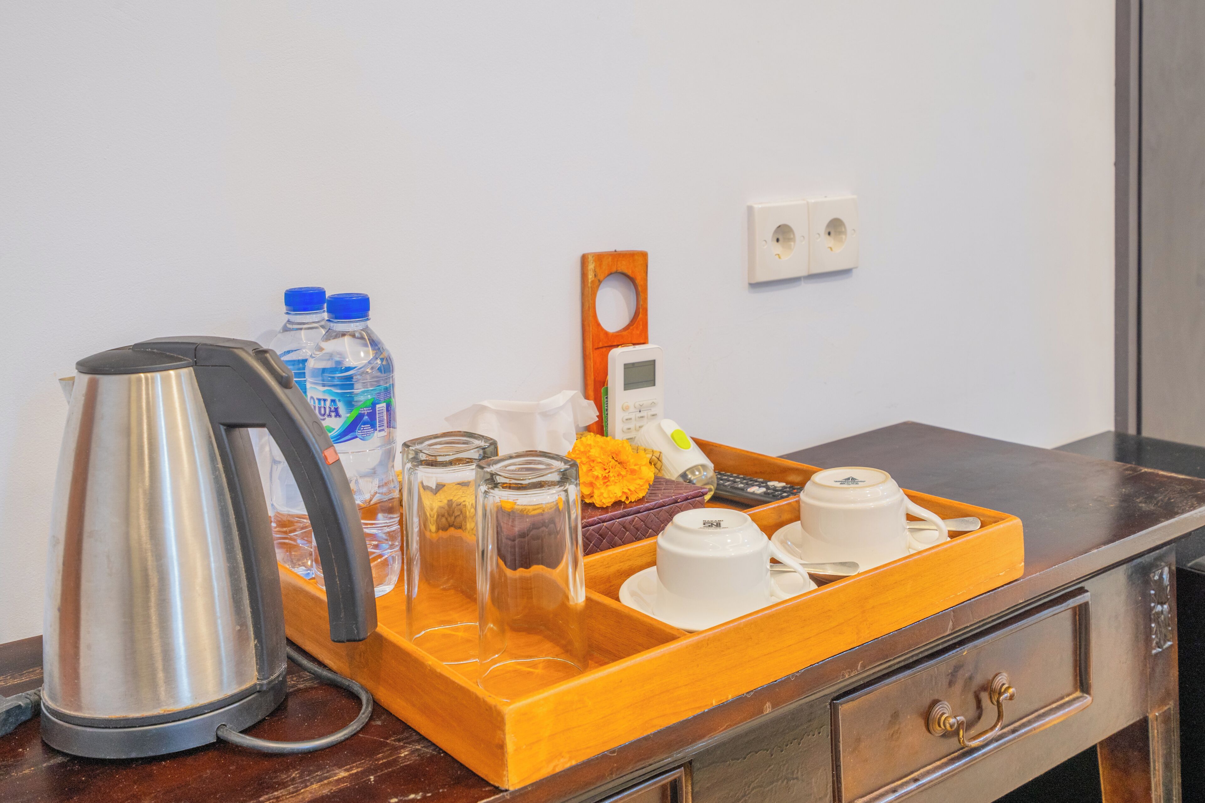 A tray with a kettle, water bottles, a phone, a remote, and a tray of cups and saucers.