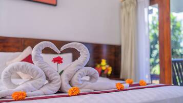 A bed with a heart-shaped towel arrangement and a single red flower.
