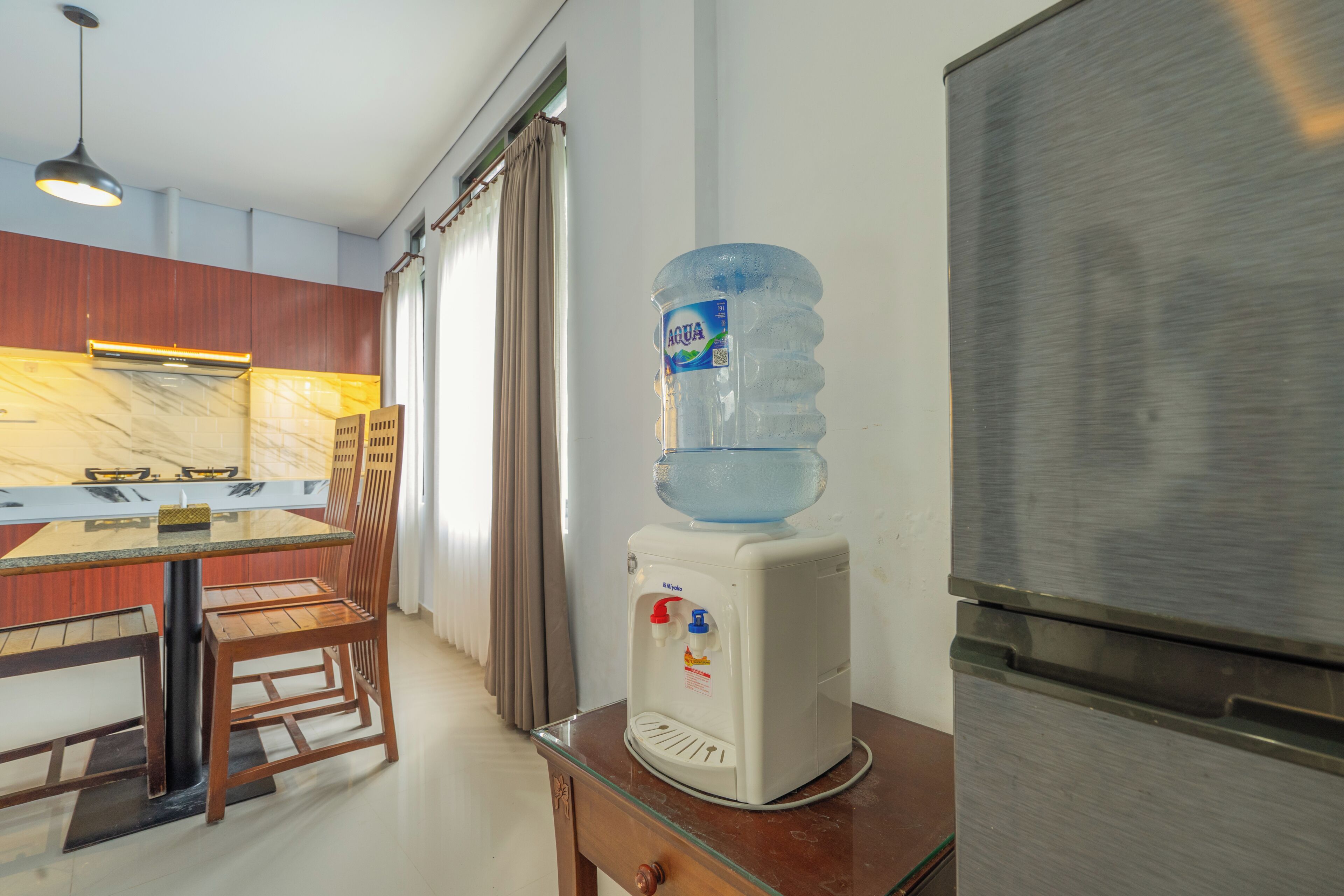 A kitchen with a water dispenser, a dining table with chairs, and a refrigerator.