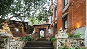 A staircase leading to a building entrance, flanked by statues and surrounded by greenery. - DWM Mandhasativa Homestay By Reccoma (Sawan)