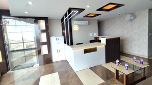 A modern reception area with a reception desk, seating, and a glass partition. - hotel PS Residency (Dehradun)