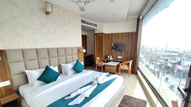 A hotel room with a large bed, a desk, a chair, a television, and a city view. - hotel PS Residency (Dehradun)