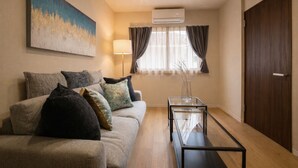 A modern living room with a sofa, a glass coffee table, a painting on the wall, an air conditioning unit, and a door. - KISEN KOBE EKIMAE (Kobe)