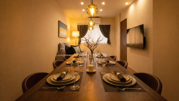 A dining area with a long table set for four, a vase with branches, and a modern pendant light. - KISEN KOBE EKIMAE (Kobe)