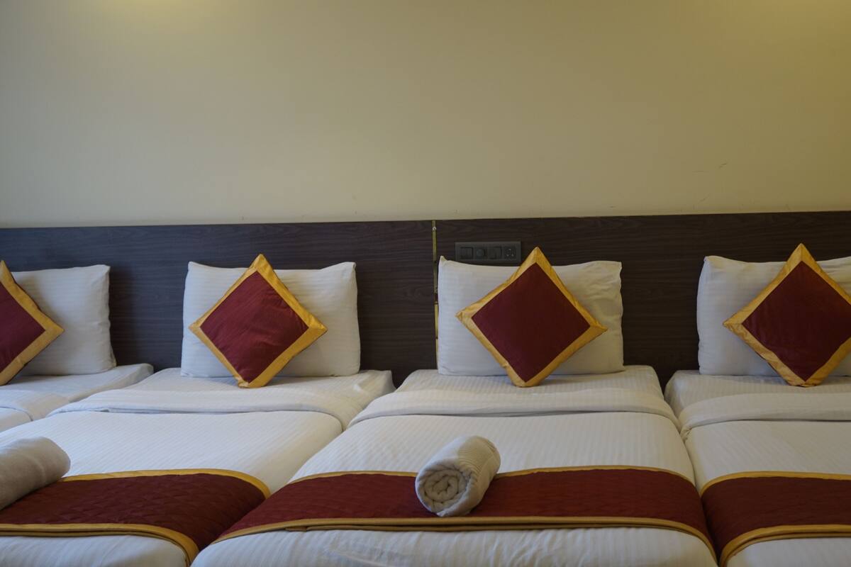 A hotel room with four beds, each with white bedding and red diamond-patterned pillows.
