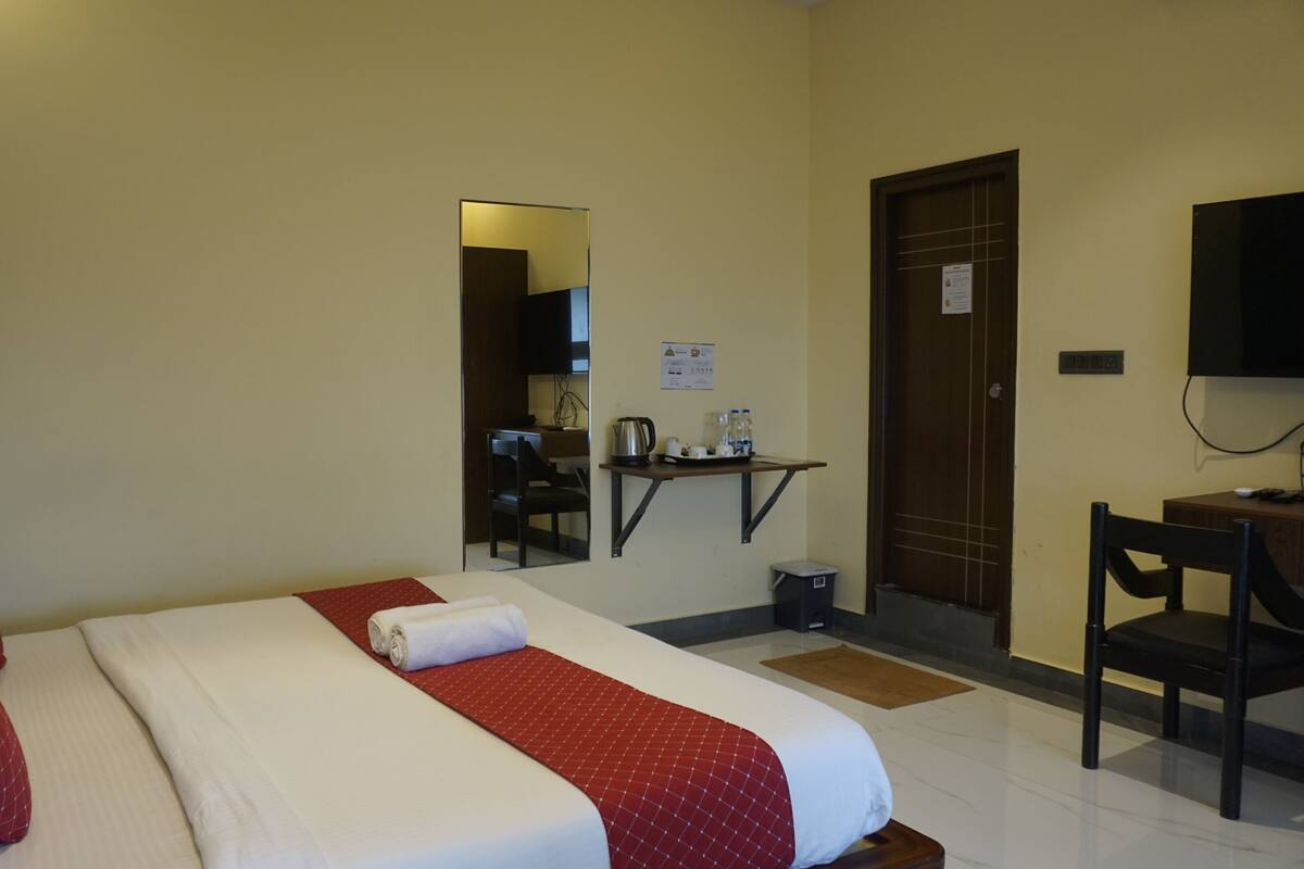 A hotel room with a bed, a desk, a chair, a television, and a small kitchenette area.