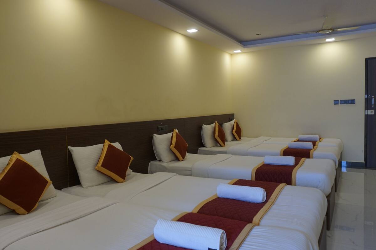 A hotel room with four beds arranged in a row, each with white bedding and red accents.