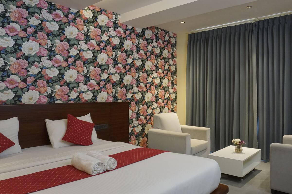A hotel room with a large bed, a chair, a small table, and a floral wallpaper.