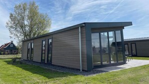 A modern building with large windows, a flat roof, and a gravel driveway. - Modern chalet with 2 bathrooms (West-Graftdijk)