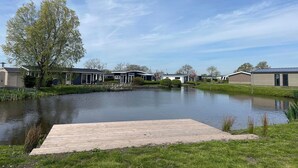 A lakeside view with a wooden dock, a pond, and several modern buildings. - Modern chalet with 2 bathrooms (West-Graftdijk)