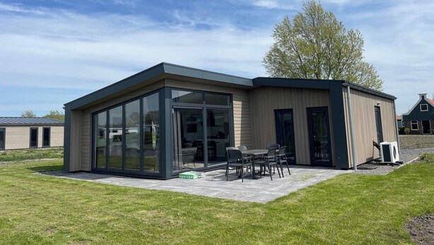 A modern building with large glass doors, a patio with outdoor seating, and a tree nearby. - Modern chalet with 2 bathrooms (West-Graftdijk)
