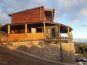 Una casa de madera de dos pisos con balcón, cimientos de piedra y vistas al paisaje.