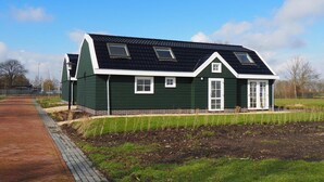A green house with a sloped roof, multiple windows, and a paved pathway leading to it.