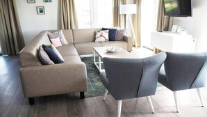 A modern living room with a sofa, two chairs, a coffee table, a TV, and a white console.