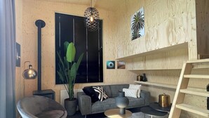 Ein modernes Wohnzimmer mit einem grauen Sofa, einem runden Couchtisch, einem grauen Sessel, einer Holztreppe und einem großen Fenster mit Jalousien.