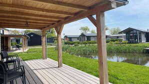 Ein überdachter Außenbereich mit Holzterrasse, Teich und Blick auf umliegende Gebäude.