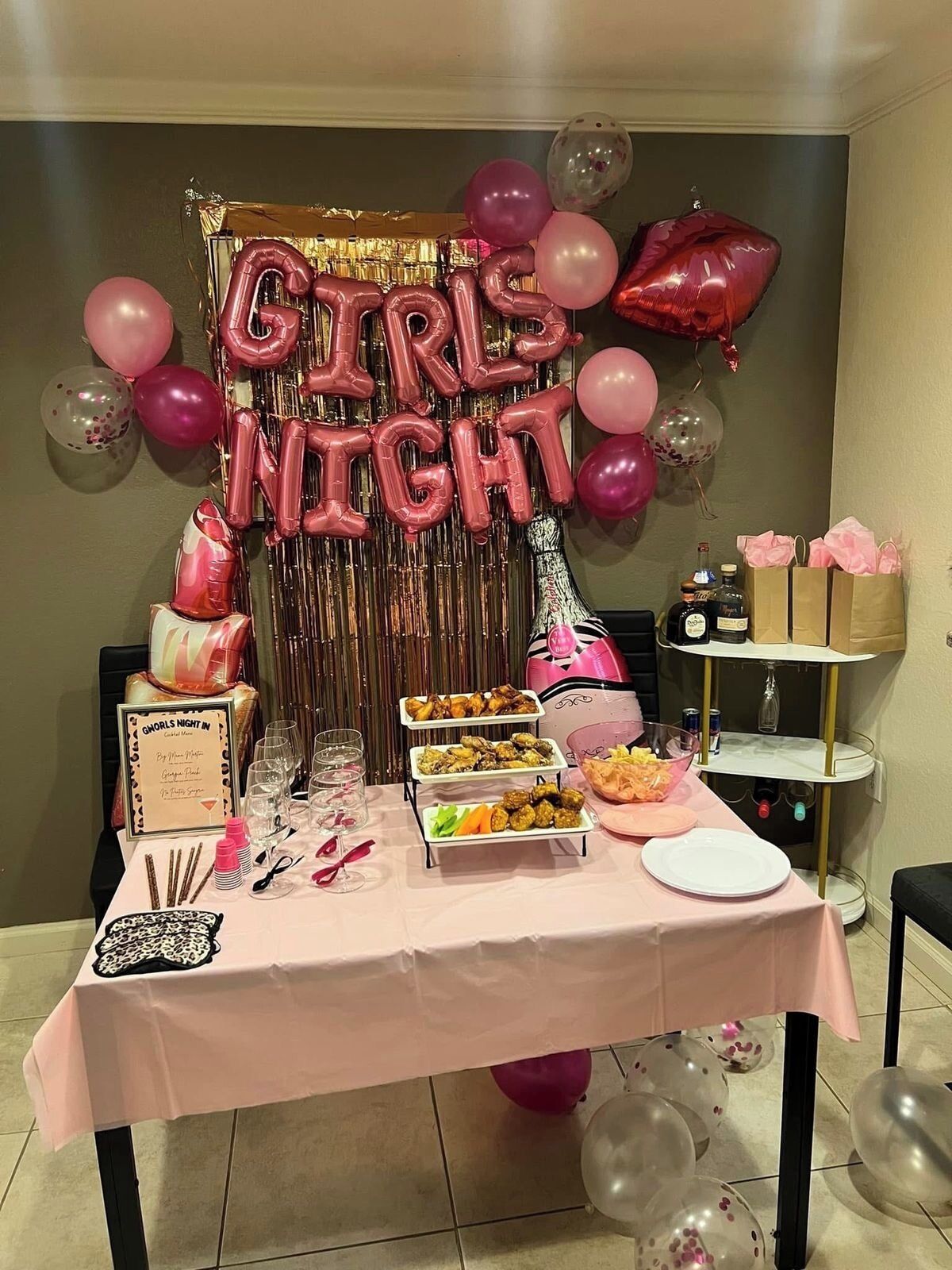 A table set up with a 'Girls Night' theme, including balloons, a banner, and various snacks.
