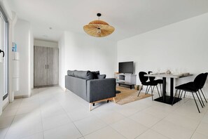 A modern living room with a grey sofa, a dining table with black chairs, a TV, and a unique ceiling light fixture. - Elegant Appt - 1BDR/2P - Near Paris & La Défense (Suresnes)