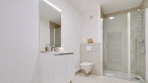 Moderni kylpyhuone, jossa on lasiseinällä varustettu suihku, wc ja peilillä varustettu pesuallas.