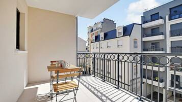 A balcony with a wooden table and chairs, a metal railing, and a view of neighboring buildings.