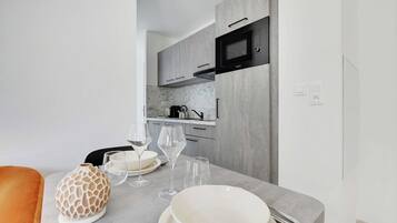A modern kitchen with grey cabinets, a microwave, and a countertop with a vase, wine glasses, and plates.