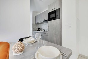 A modern kitchen with grey cabinets, a microwave, and a countertop with a vase, wine glasses, and plates. - Elegant Appt - 1BDR/2P - Near Paris & La Défense (Suresnes)