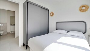 Ein modernes Schlafzimmer mit Bett, Kleiderschrank und einem durch eine offene Tür einsehbaren Badezimmer.