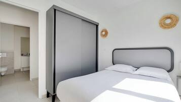 A modern bedroom with a bed, a wardrobe, and a bathroom visible through an open door.