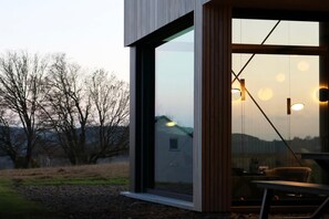 A modern building with large windows, a dining area with a table and chairs, and hanging pendant lights. - Modern design house with sauna 'Arduenna Silva' (La Roche-en-Ardenne)