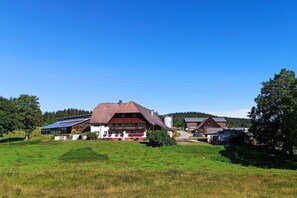 Ein ländliches Haus mit Satteldach, einer Solaranlage und einem Bauernhof im Hintergrund.