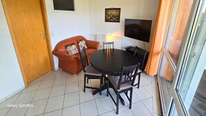 En kompakt opholdsstue med sofa, spisebord, stole, fjernsyn og en dør.
