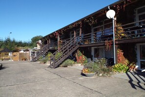 A building with a staircase leading to a balcony, surrounded by potted plants and a clear sky.
