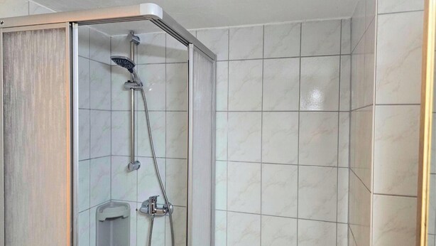 Une douche avec une porte en verre, un pommeau de douche à main et un robinet mural.