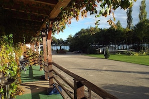 A covered outdoor area with a wooden fence, a concrete path, and a view of a body of water in the background.