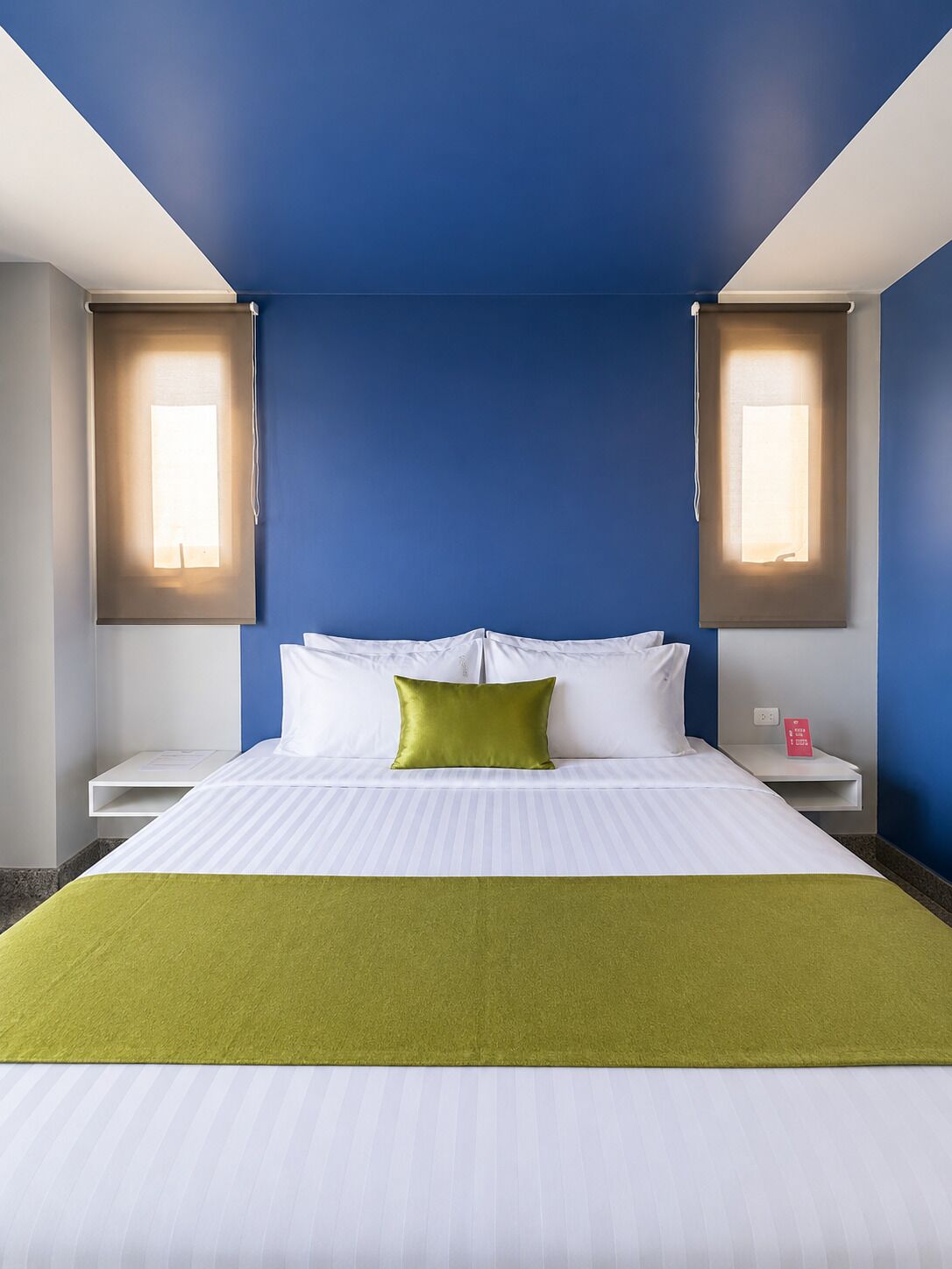 Hotelkamer met een bed, twee nachtkastjes, een sprei en twee wandlampen.