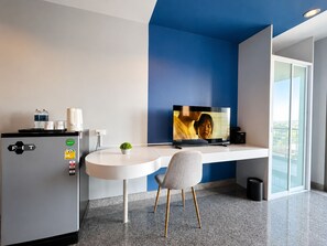 A modern hotel room with a white desk, a television, a minibar, and a view of the city. - iCheck inn Phuket Town (Phuket)