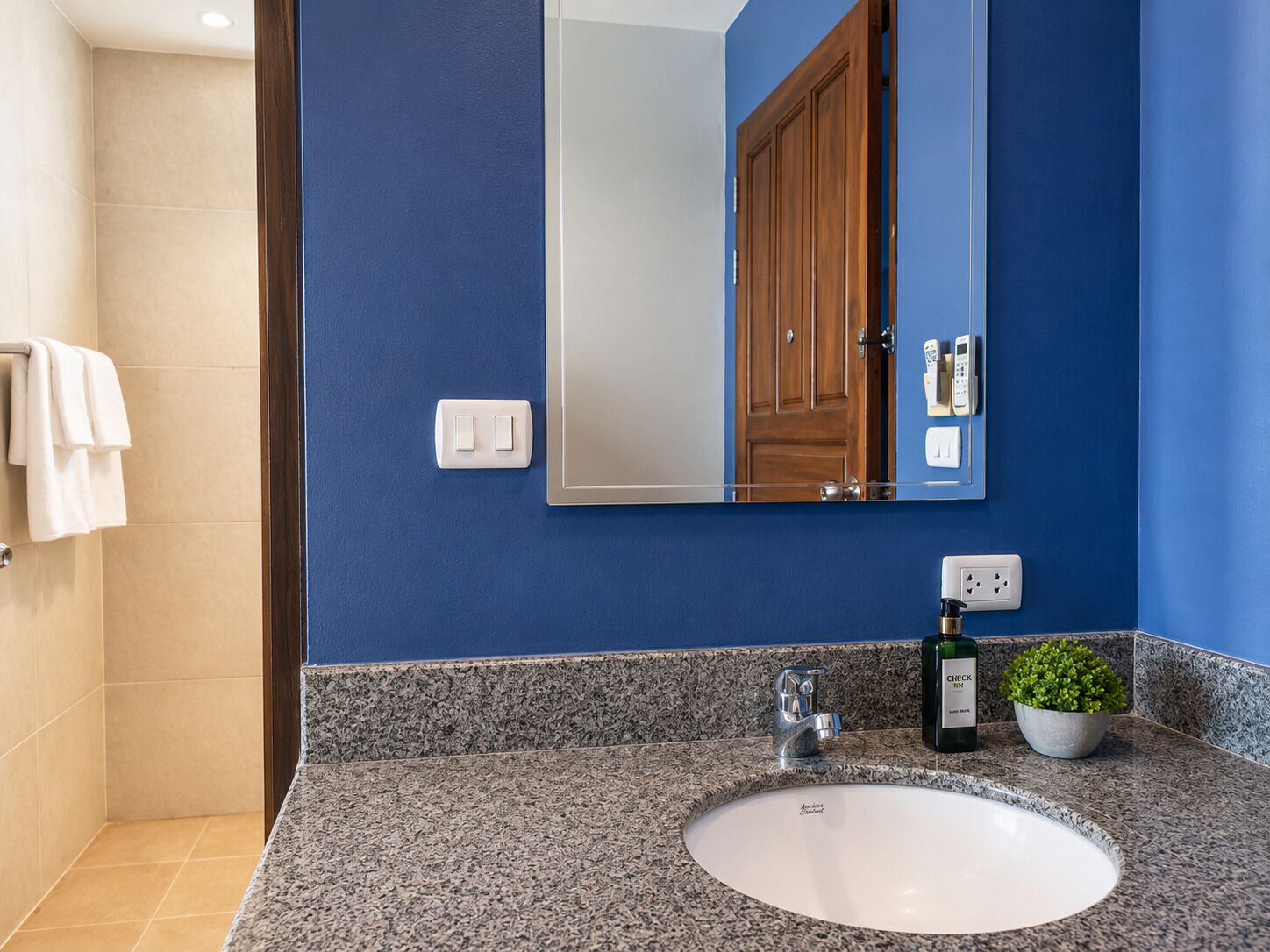 A bathroom with a blue wall, a white sink, a mirror, a wooden door, and a towel rack.