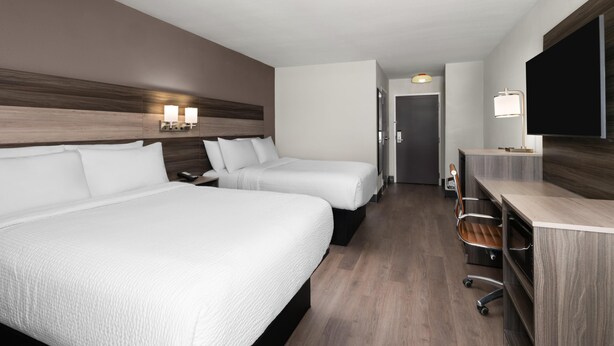 A hotel room with two beds, a desk, a TV, and a door leading to a hallway. - Augusta West (Augusta)