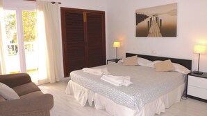 Un dormitorio con una cama, dos lámparas de noche, una silla, un armario y un cuadro en la pared.