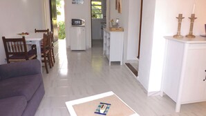 Una sala de estar con sofá, una mesa de centro, un comedor con sillas, una cocina con microondas y un pasillo que conduce a una puerta.