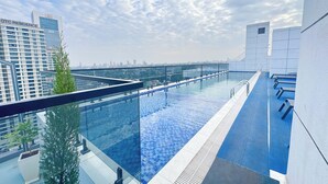 Una piscina a sfioro sul tetto con una barriera in vetro, uno skyline cittadino sullo sfondo e un edificio moderno con il cartello 'GTC Residence'.