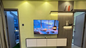 Een moderne woonkamer met een grote flatscreen-tv, twee ronde houten tafels, een inbouwmeubel en een open haard.