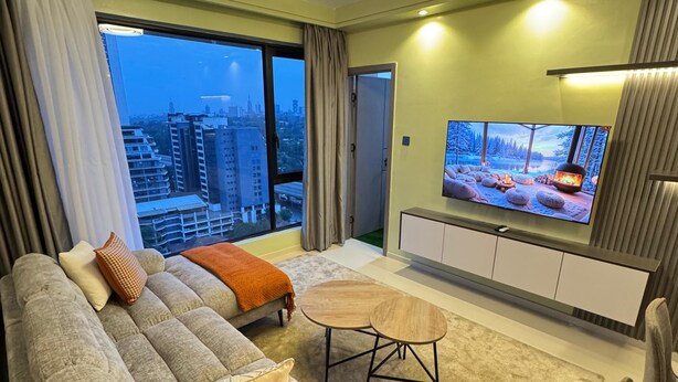 Een moderne woonkamer met een grote bank, een televisie en uitzicht op de stad.