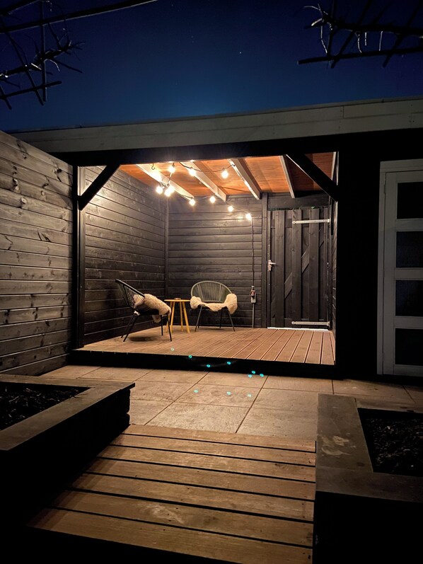 A wooden deck with a bench and chairs, a small table, and string lights.