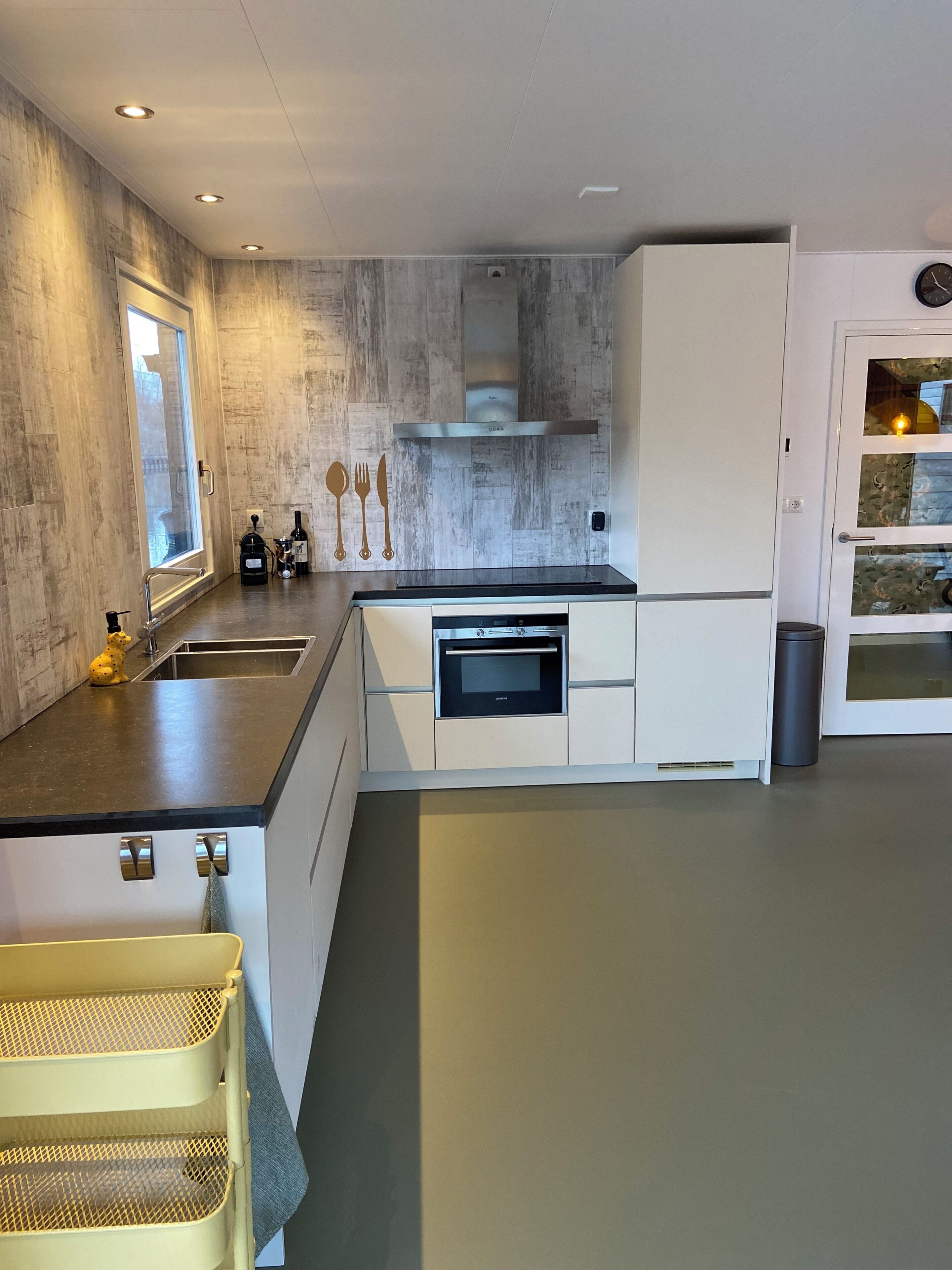 Een moderne keuken met een inbouwoven, roestvrijstalen apparatuur en een raam.