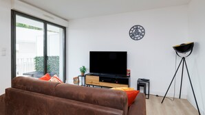 En moderne stue med sofa, fjernsyn, stativ og et ur på væggen.