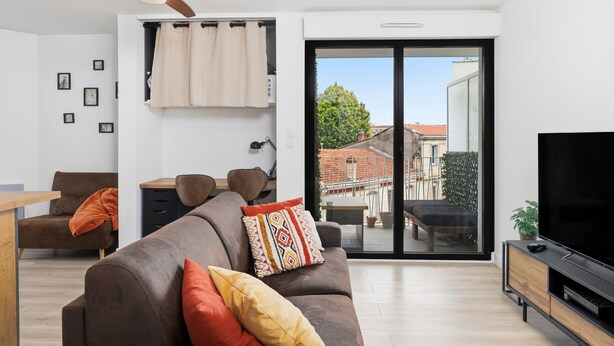 En moderne stue med sofa, fjernsyn, loftventilator og en skydedør til et udendørs område.