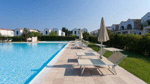 A swimming pool with lounge chairs and umbrellas, surrounded by greenery and white buildings with red roofs. - Blumare Apartment 3 Pool & Sea (Otranto)