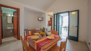 A dining area with a table set for four, a kitchen in the background, and a sliding glass door leading to an outdoor patio. - Blumare Apartment 3 Pool & Sea (Otranto)
