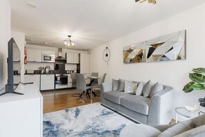 A modern living room with a grey sofa, a coffee table, and a dining area with chairs and a table. - Beautifully Presented 2BDR Flat in Canada Water (Greater London)
